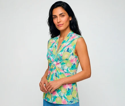 Femme portant un chemisier Olsen sans manches à motif fruité et floral coloré vert, rose et sarcelle, avec un col en V et un anneau décoratif à l'avant.