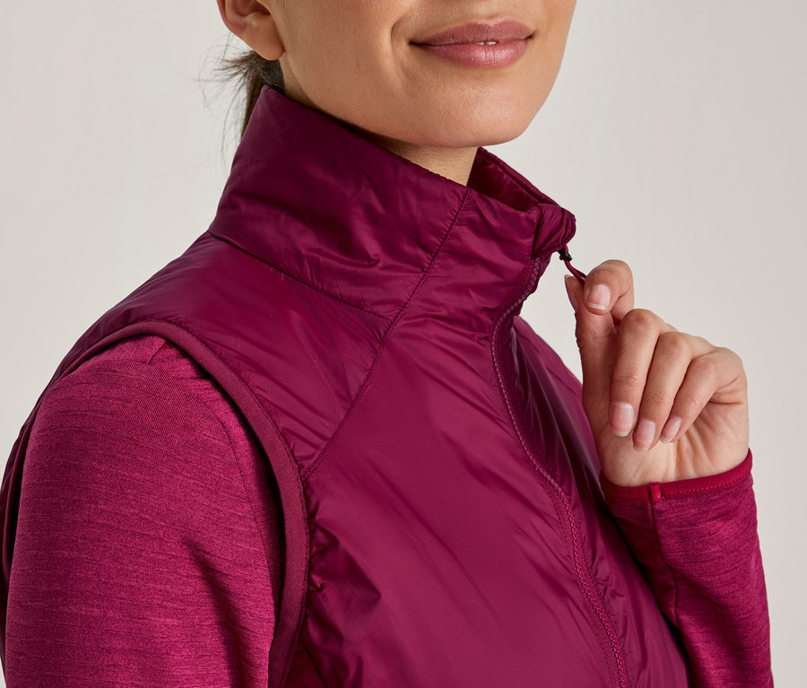 Femme portant un haut à manches longues et un gilet sans manches matelassé rose foncé, tirant sur la fermeture éclair du gilet.