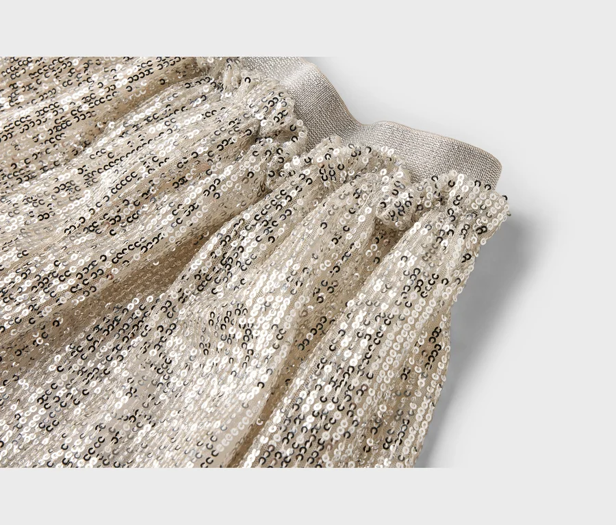 Gros plan d'un vêtement en tissu doré clair recouvert de petites paillettes argentées brillantes, avec une taille élastique froncée.