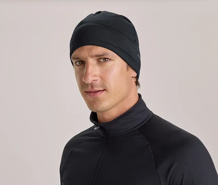 Un homme portant un bonnet noir et un haut noir à manches longues avec un col montant et une fermeture éclair, regarde directement l'objectif.