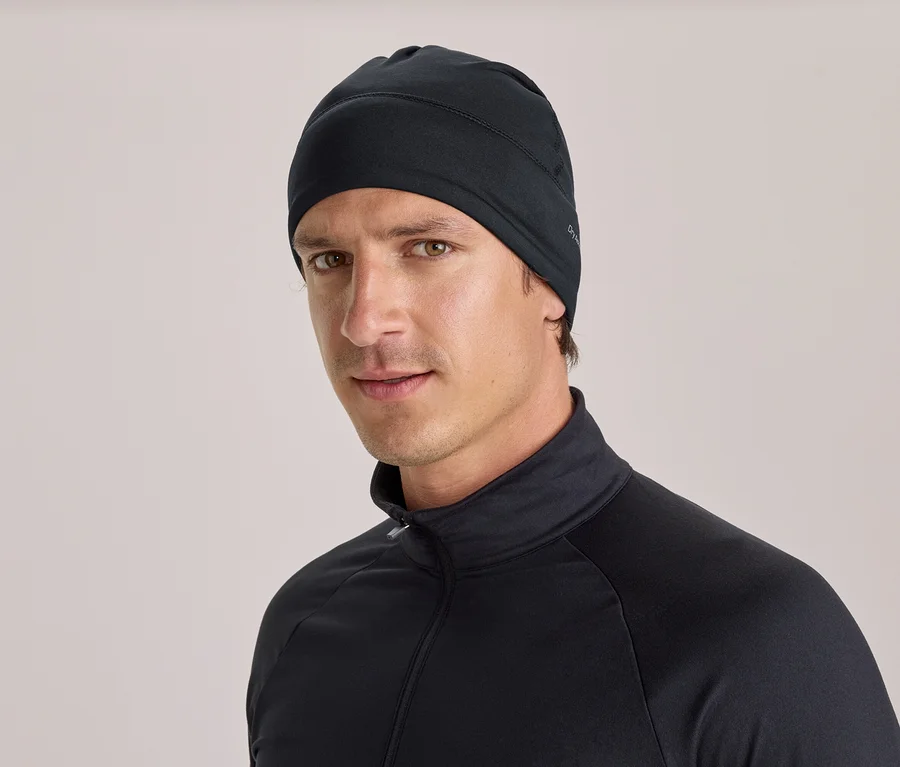 Un homme portant un bonnet noir et un haut noir à manches longues avec un col montant et une fermeture éclair, regarde directement l'objectif.
