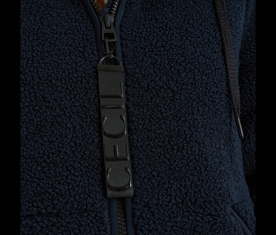 Gros plan sur une veste CECIL bleu foncé en matière polaire, avec fermeture éclair, tirette et étiquette en tissu avec le logo CECIL.
