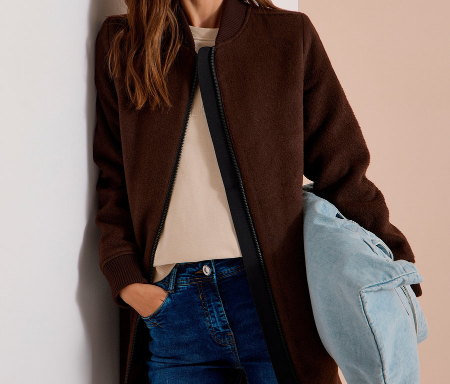Femme portant un blouson CECIL marron, un haut beige clair et un jean bleu, tenant un sac bleu clair.