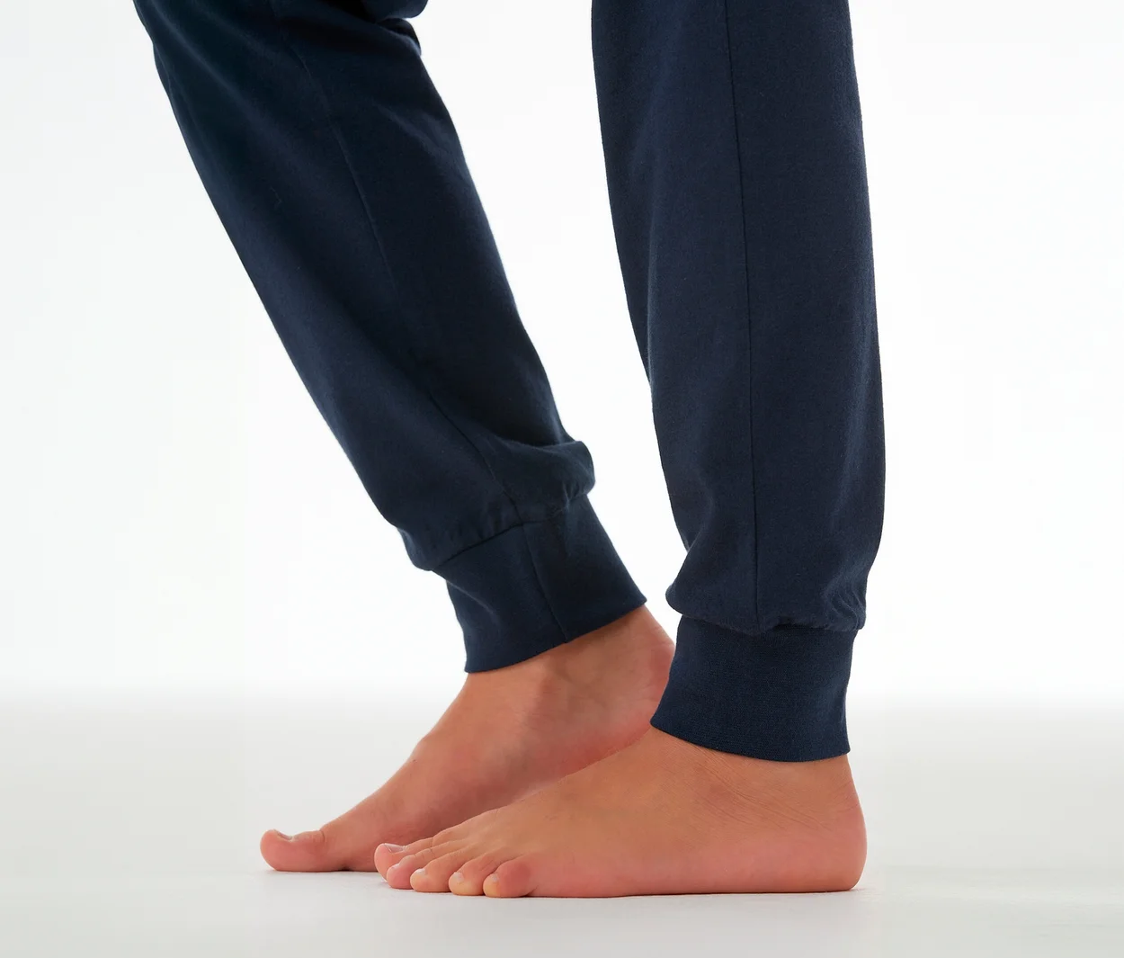 Jambes d'enfant portant un pantalon de pyjama SCHIESSER bleu marine avec des chevilles resserrées, pieds nus.