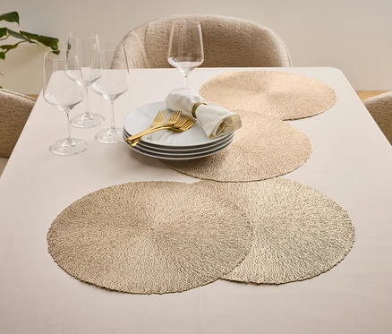 Table dressée avec assiettes, couverts dorés, verres et sets de table.