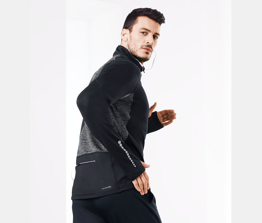 Homme portant un T-shirt de sport thermique noir et des écouteurs regardant par-dessus son épaule.