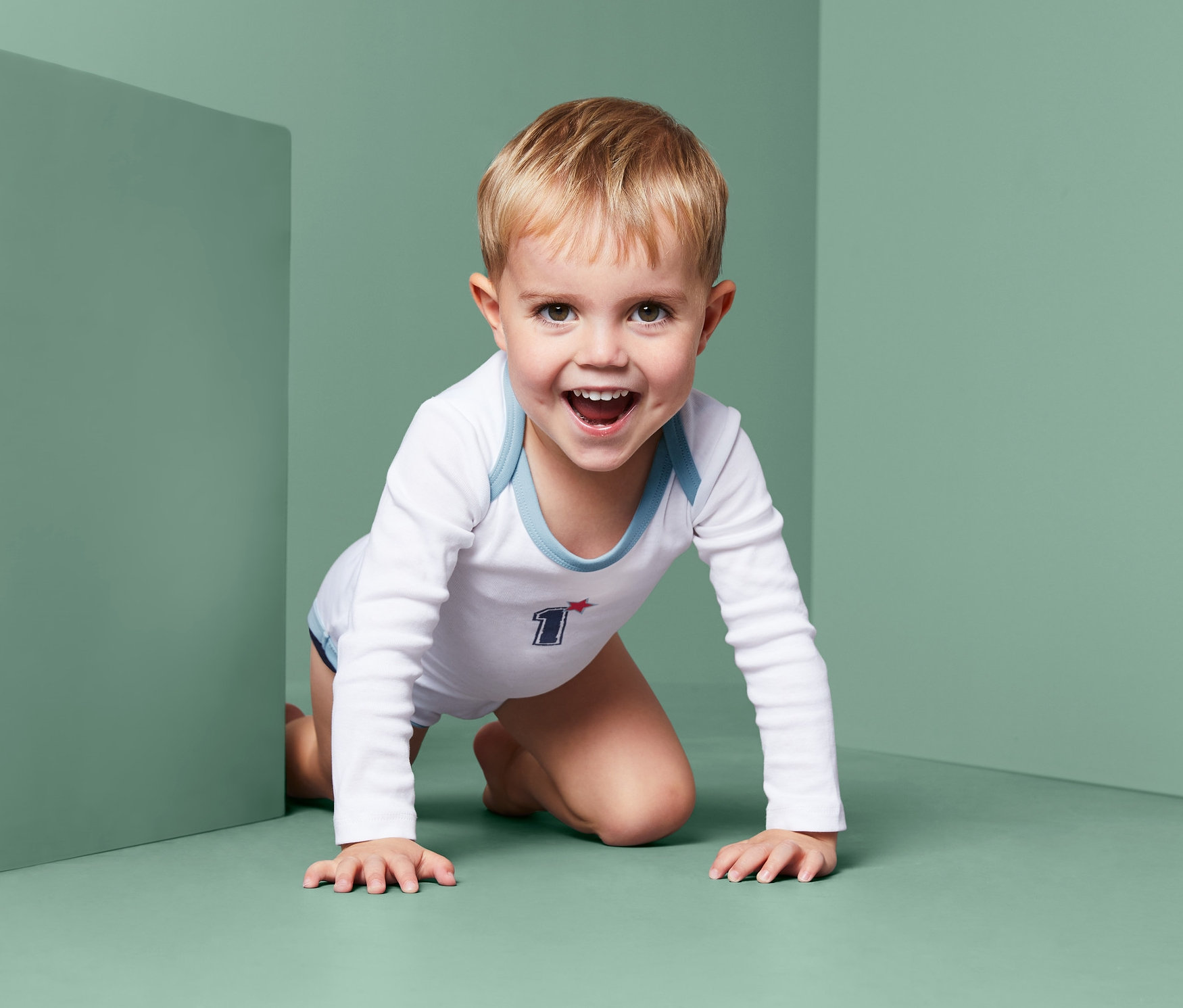 Un enfant rampe sur le sol et porte un des 3 bodys à manches longues.