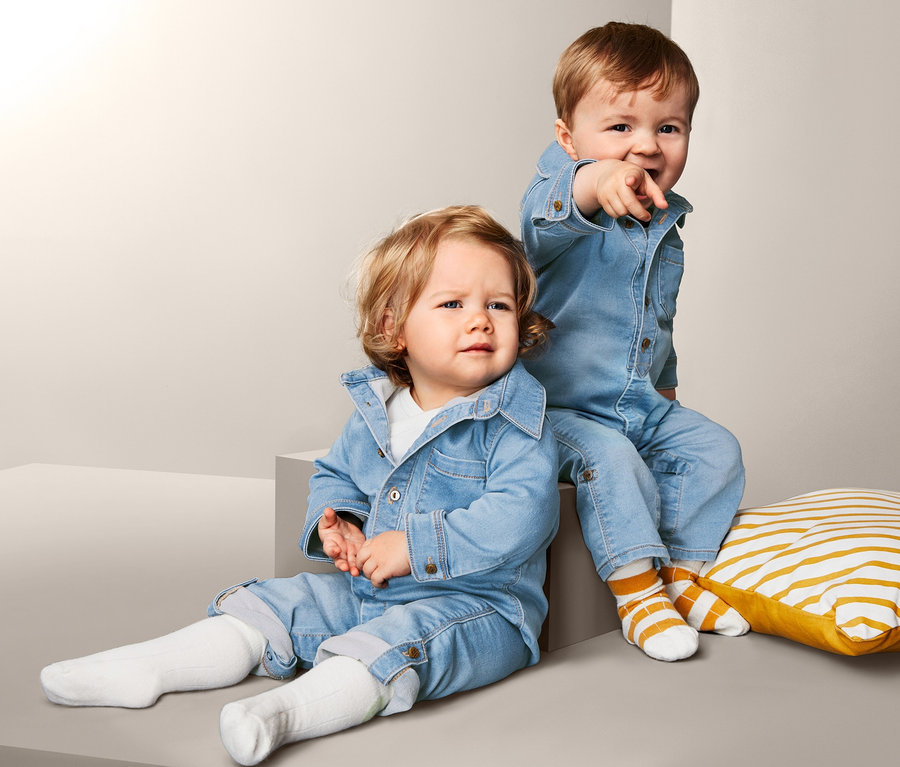 Deux jeunes enfants posent sur un fond gris. Les deux portent une combinaison en denim stretch.