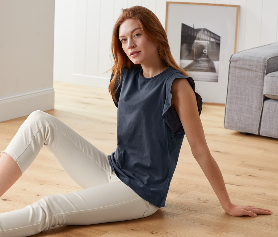 Femme assise par terre portant un top bleu marine EarthColors® et un pantalon blanc.