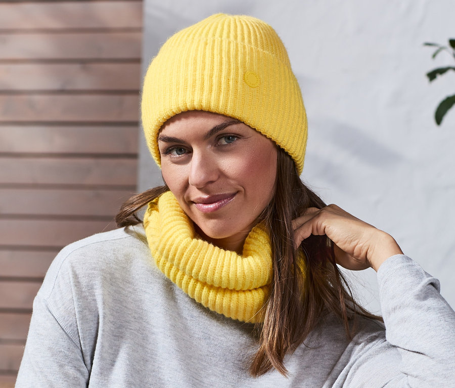 Femme assise sur un banc avec un bonnet en maille jaune.
