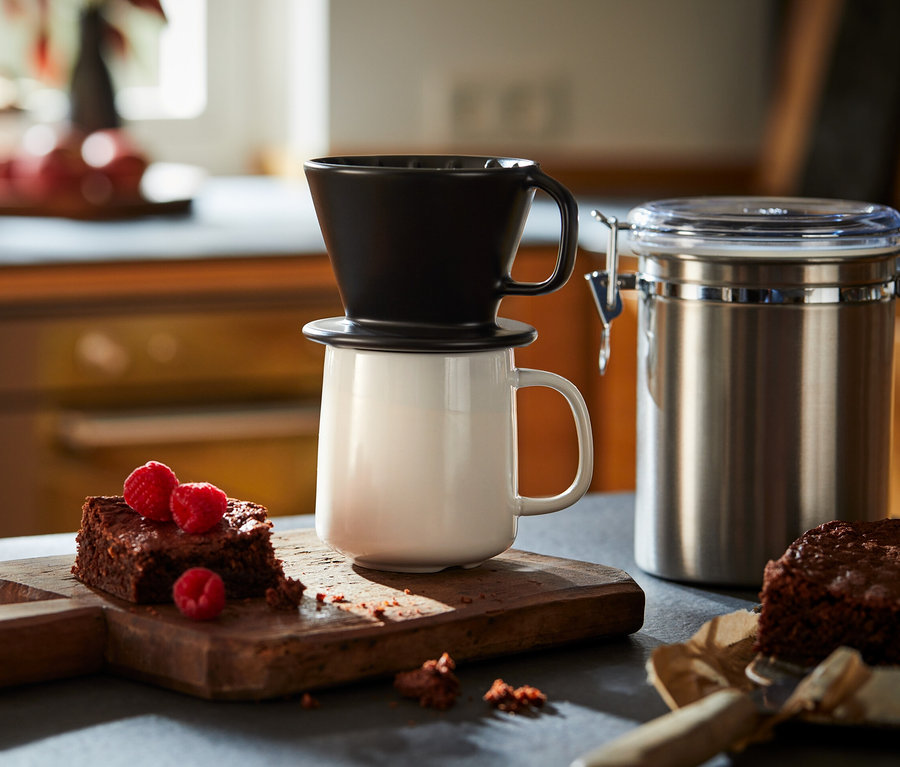 Un filtre à café manuel noir de taille 101 repose sur une tasse blanche à côté de brownies aux framboises sur une planche à découper en bois.