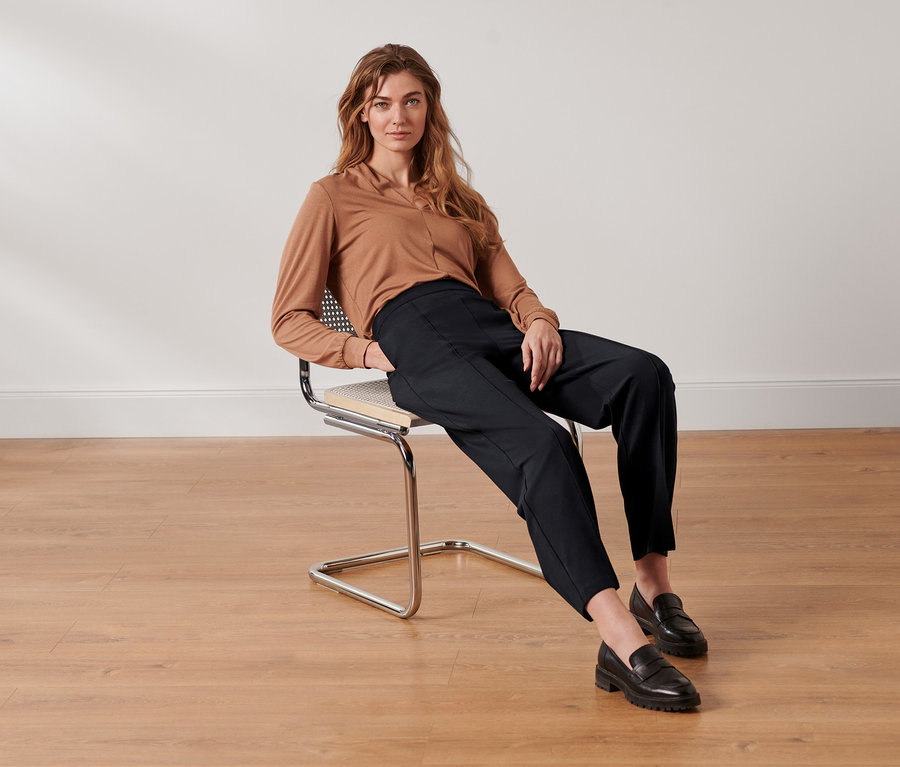 Femme assise sur une chaise portant un pantalon en jersey noir avec nervure.