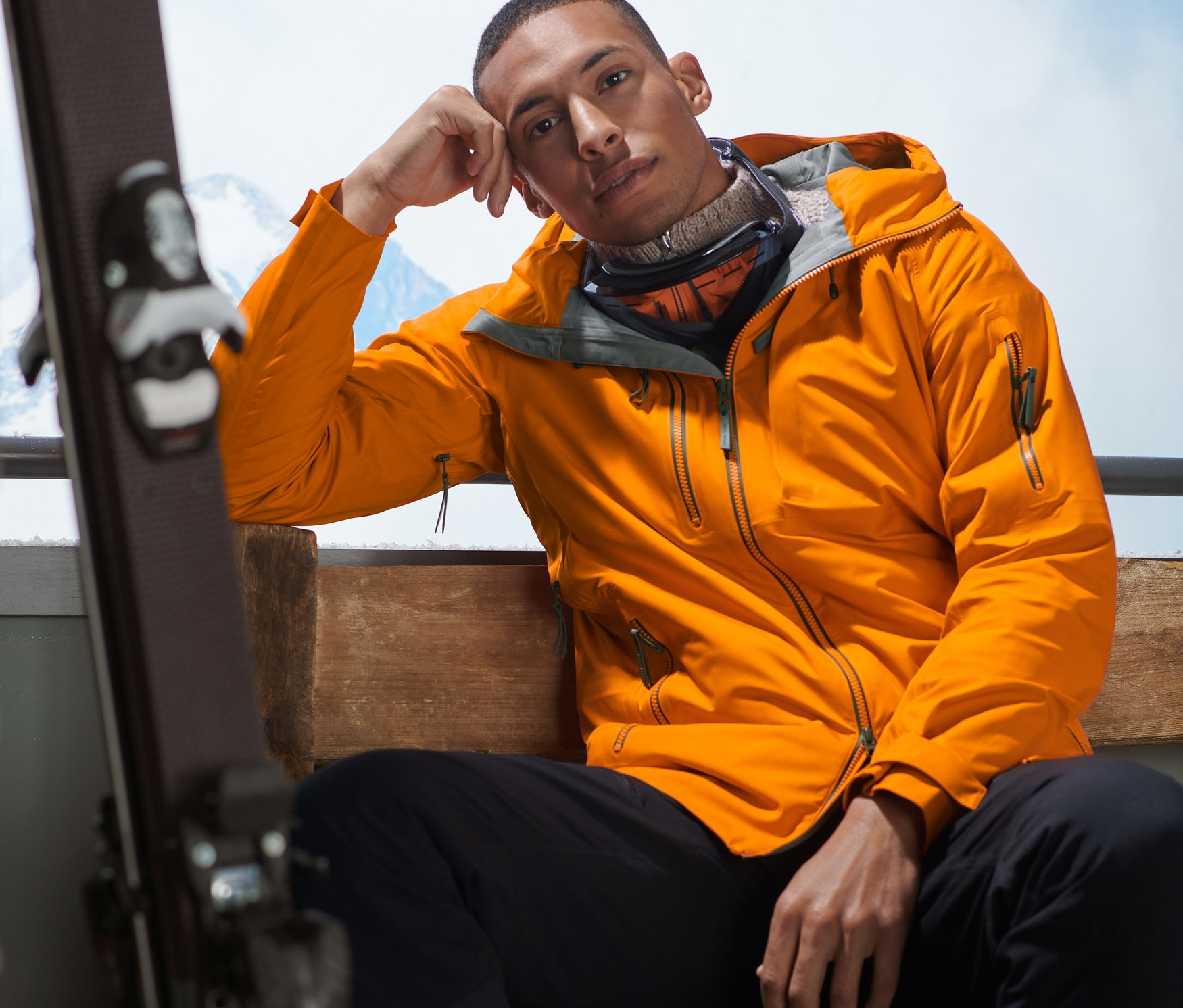 Un homme est assis sur un banc et porte une veste de ski hardshell orange.
