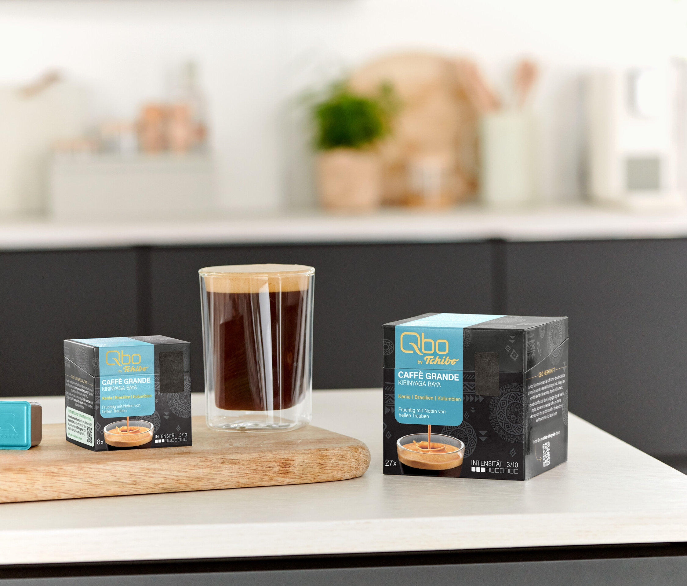 Sur une table, il y a une tasse de café, un Qbo Caffè Grande KIRINYAGA BAYA – 8 capsules et un Qbo Caffè Grande KIRINYAGA BAYA – 27 capsules.