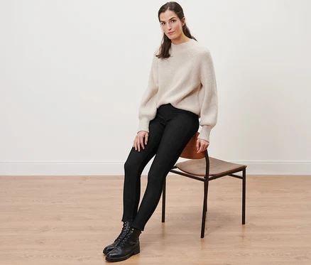 Une femme est assise sur une chaise et porte un legging doublé à l’aspect jean, un pull et des bottes.