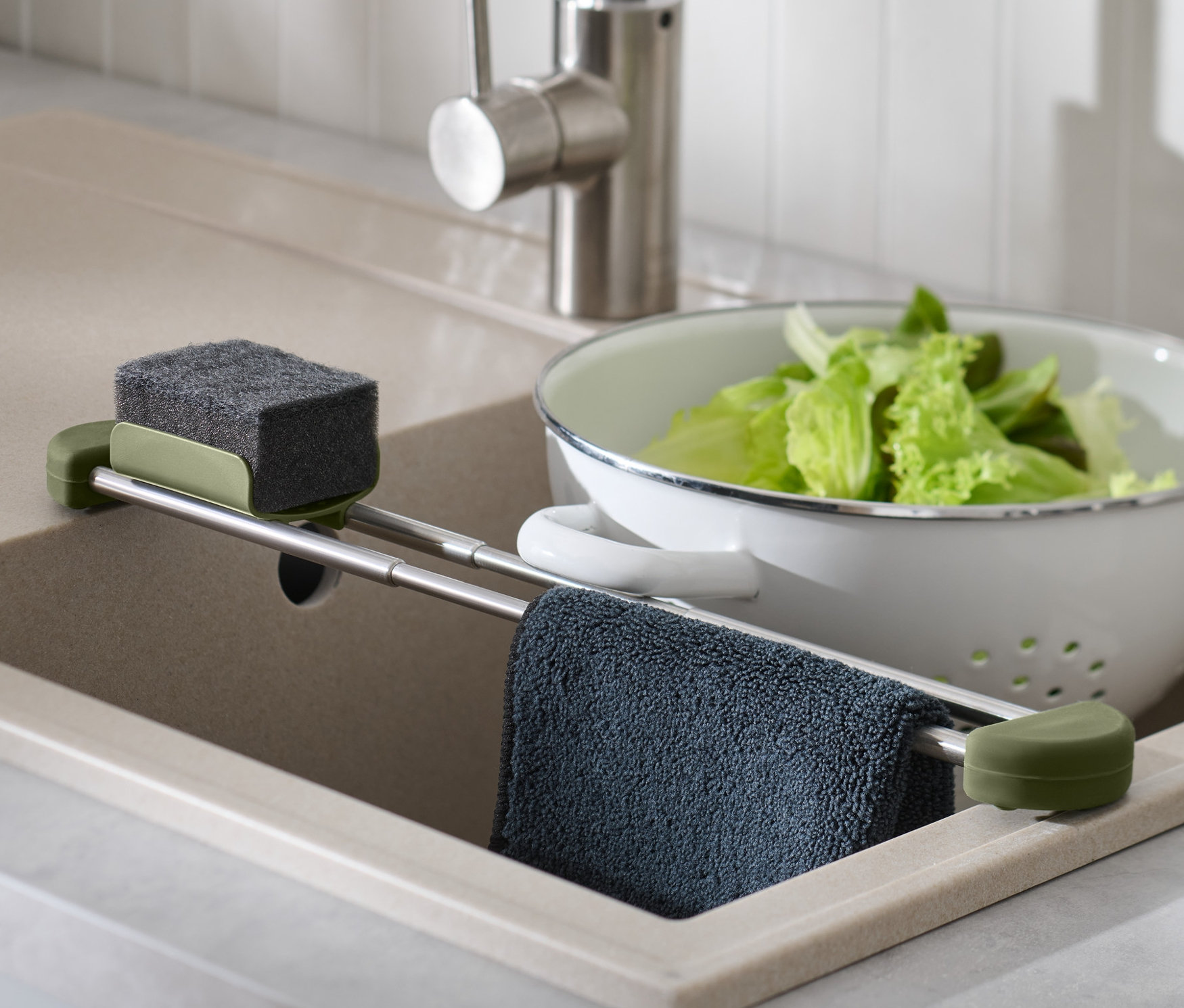 Dans l'évier, il y a un support de rangement amovible pour évier avec une éponge, un chiffon et de la salade dans une passoire.