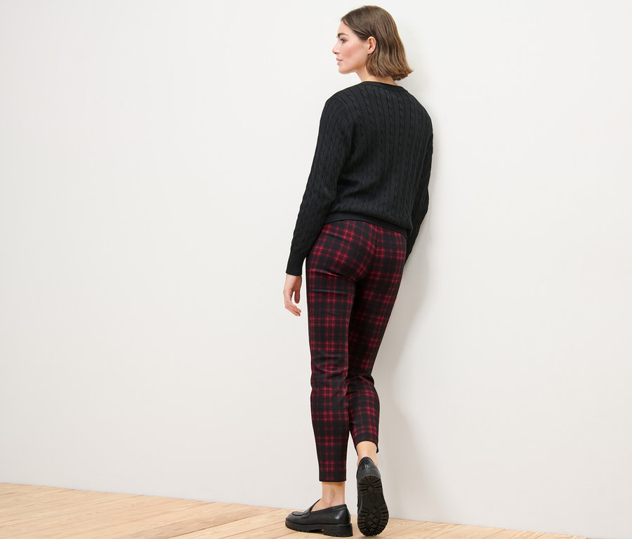 Une femme, vue de dos, porte un pantalon stretch à carreaux, un pull noir et des chaussures noires.