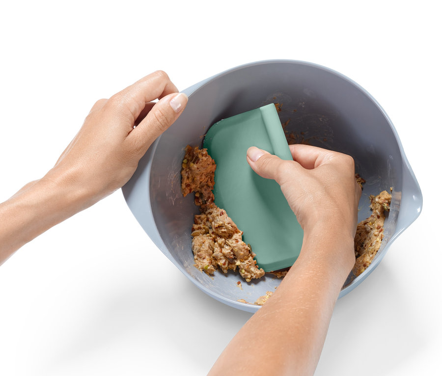 Deux mains mélangent de la pâte dans un bol avec une spatule verte du kit d'accessoires professionnels de pâtisserie.