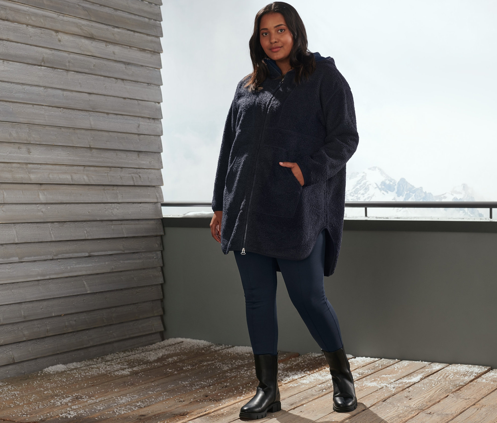 Une femme pose à l'extérieur en legging thermique bleu et un manteau oversize en peluche.