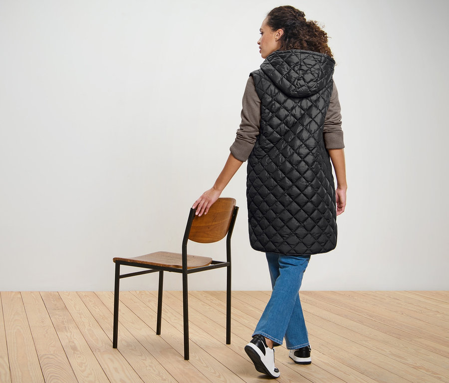 Femme posant en long gilet sans manches matelassé avec capuche.
