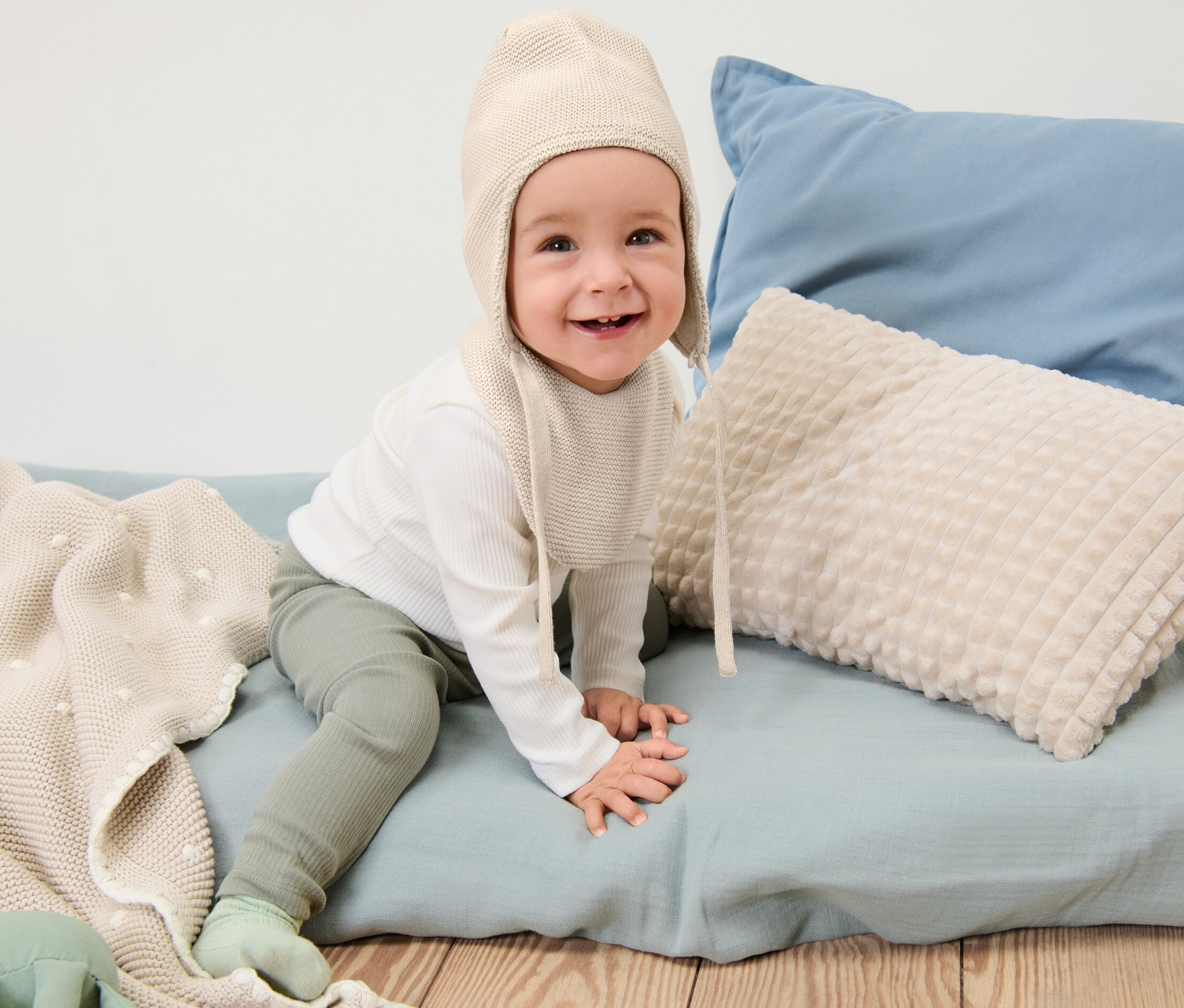 Un bébé souriant est assis et porte un bonnet et une écharpe en maille pour bébé.