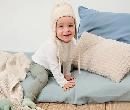 Un bébé souriant est assis et porte un bonnet et une écharpe en maille pour bébé.