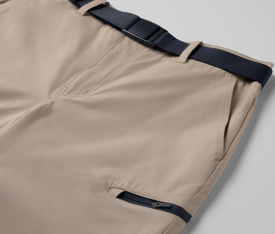 Gros plan sur un pantalon technique 2 en 1 beige avec une ceinture bleu marine et une poche zippée.