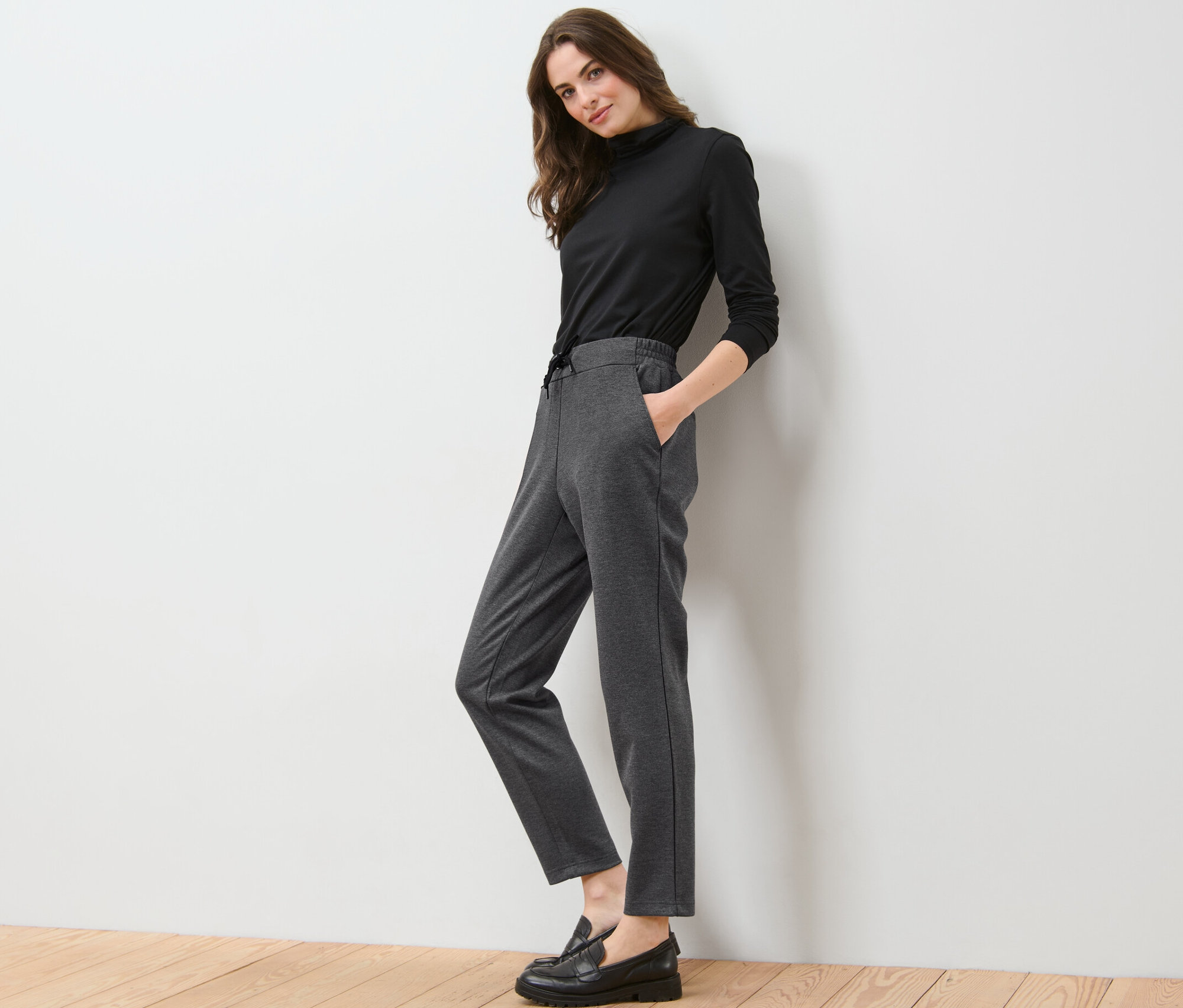 Femme posant en col roulé noir et pantalon de jogging gris.