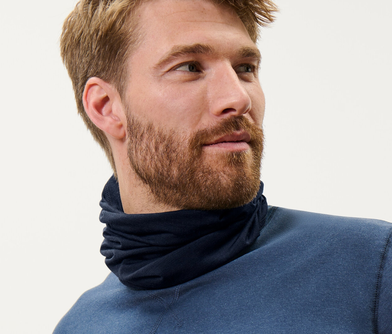 Un homme aux cheveux bruns porte un foulard multifonction bleu en laine certifiée RWS et un haut bleu.