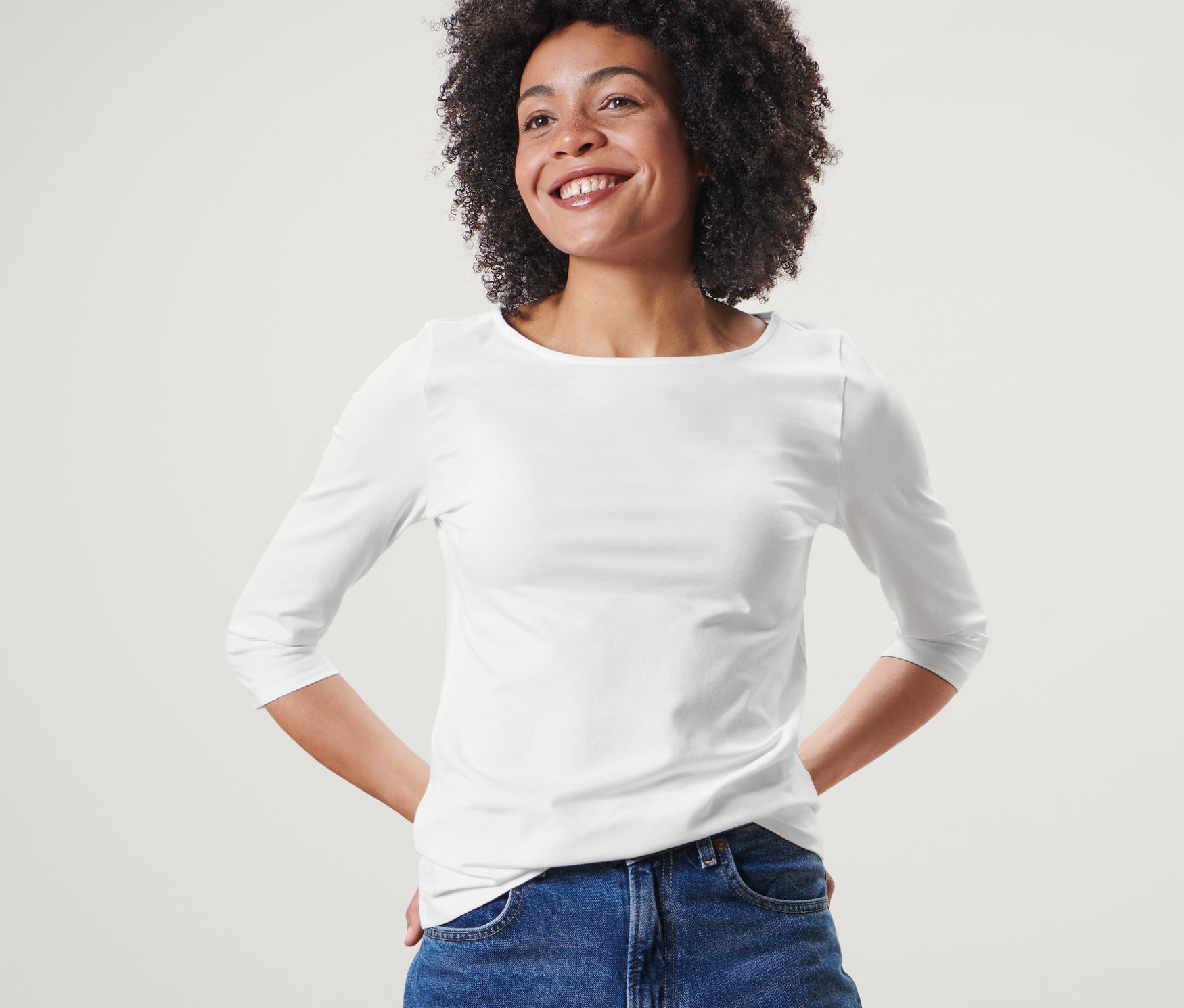 Une femme pose dans un t-shirt blanc à manches 3/4 et un jean bleu.