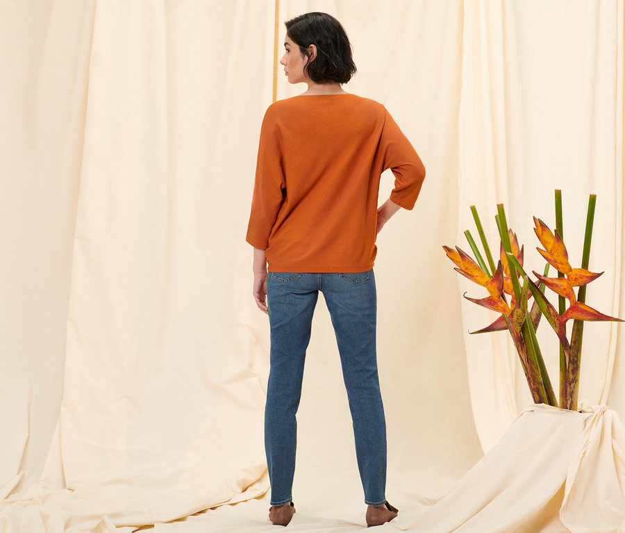 Une femme, vue de dos, porte un jean slim en denim « Fit Emma », denim bleu moyen, un pull en maille fine orange et des loafers en cuir velours.
