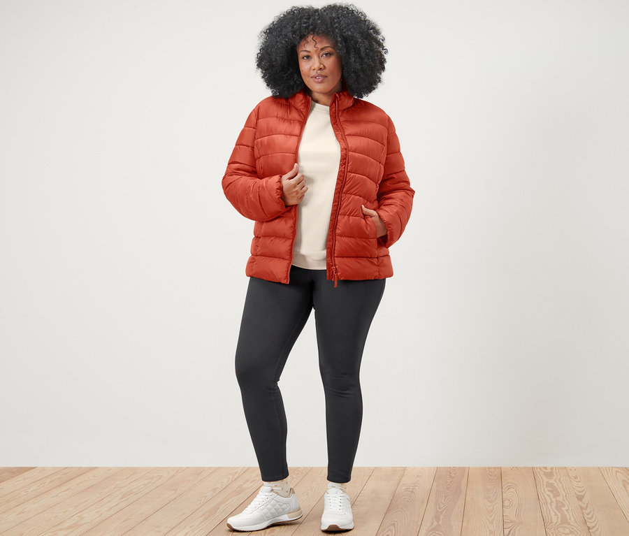 Une femme pose dans une veste surpiquée orange, un sweat-shirt avec broderie et un jegging.