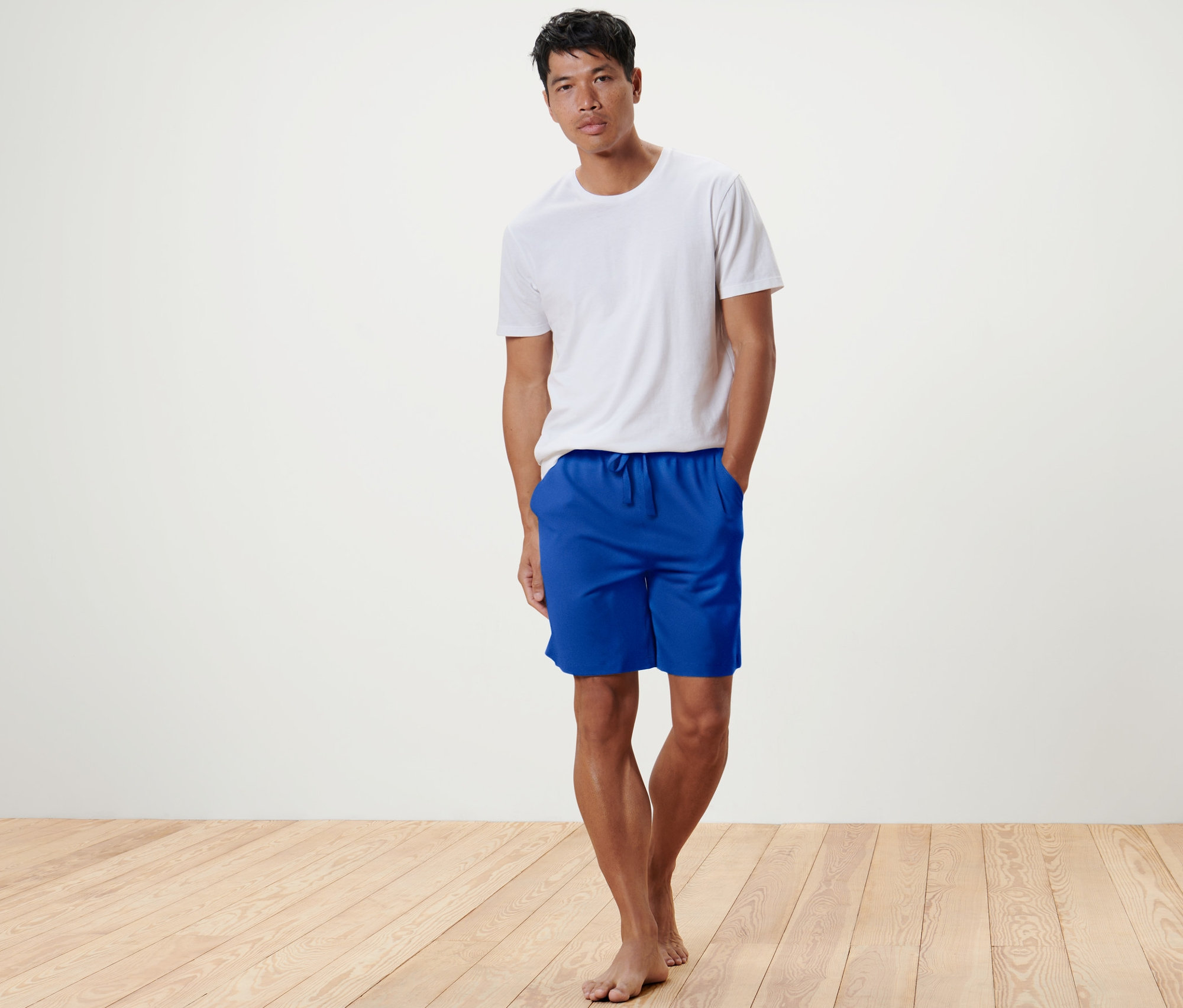 Un homme debout portant un t-shirt blanc et un short relax bleu.