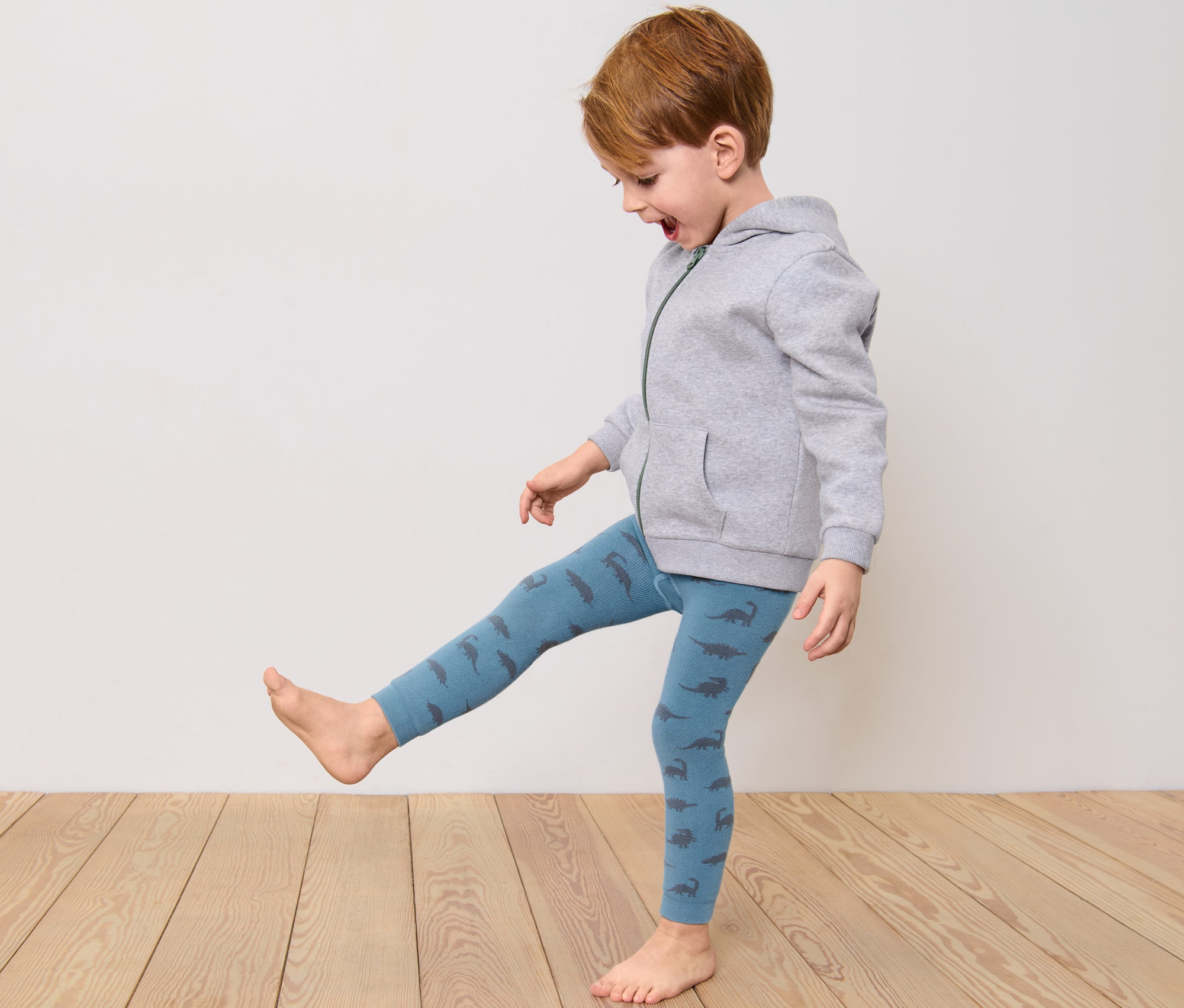 Un garçon en sweat à capuche gris et leggings thermiques bleus à motifs de dinosaures joue.
