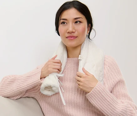 Femme assise sur un canapé tenant une bouillotte tube autour du cou.