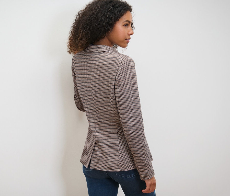 Femme posant en blazer en sweat à carreaux et jean bleu.