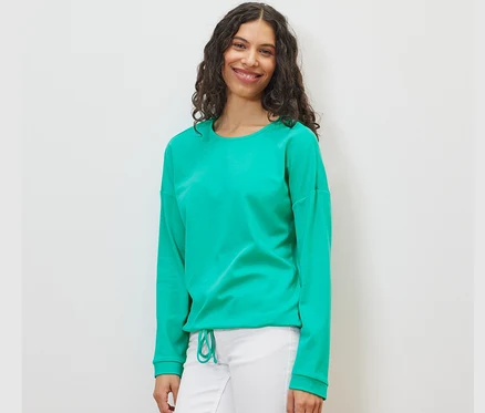 Femme portant un sweat-shirt turquoise et un pantalon blanc.