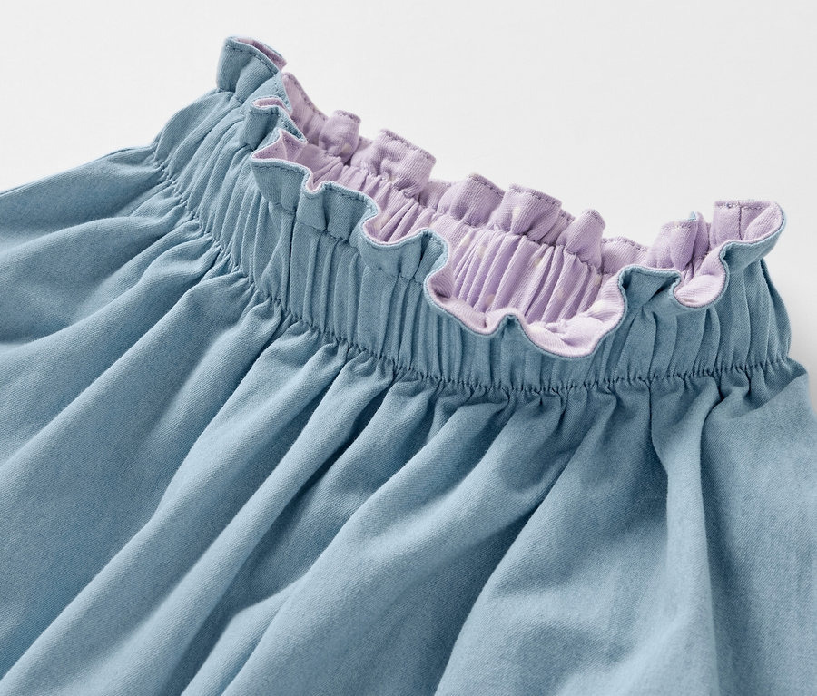 Détail d'une jupe réversible en denim pour enfants avec une ceinture à volants violets.