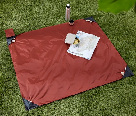 Sur l'herbe verte se trouve une mini-couverture de pique-nique avec une carte et une collation. Une bouteille thermos et une tasse sont à côté.