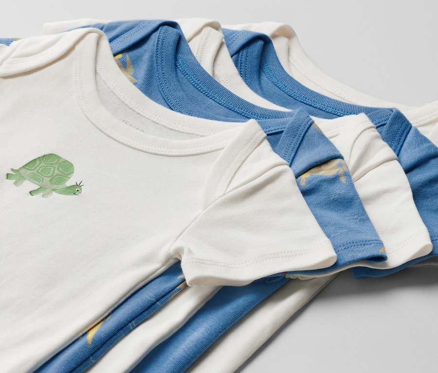 Gros plan sur cinq bodies à manches courtes pour bébé. Un body blanc est imprimé d'une tortue.