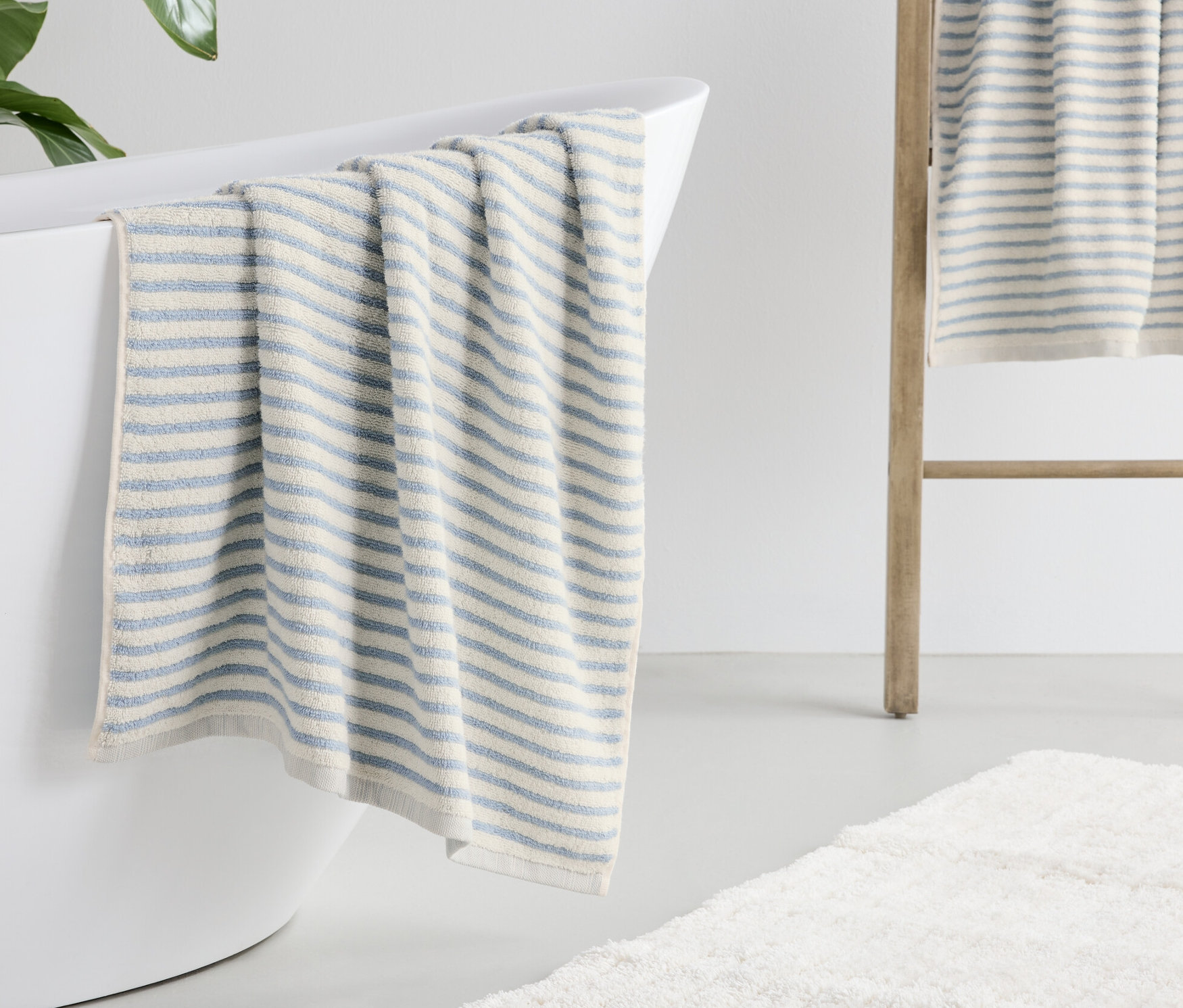 Un drap de bain rayé bleu est posé sur le bord d'une baignoire blanche.