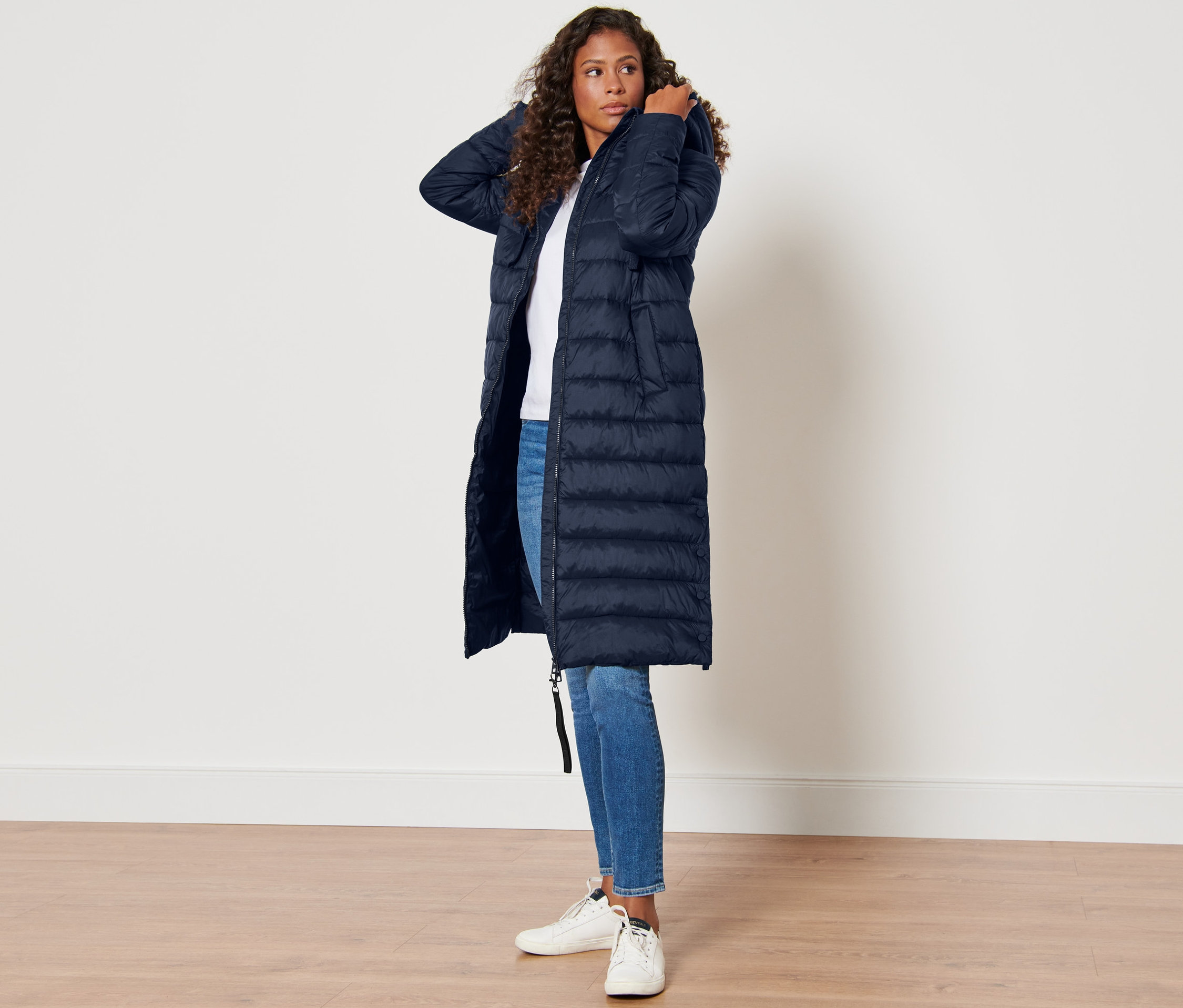 Femme posant dans un manteau matelassé à capuche bleu foncé.