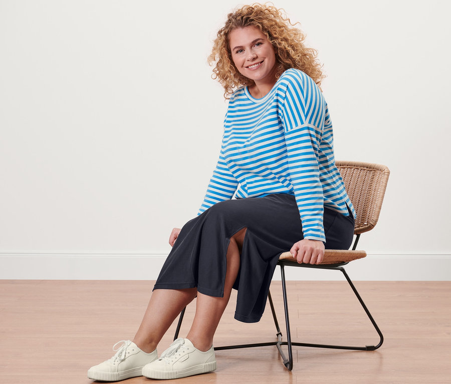 Une femme est assise sur une chaise et porte un T-shirt manches longues à rayures et une jupe en jersey piqué.