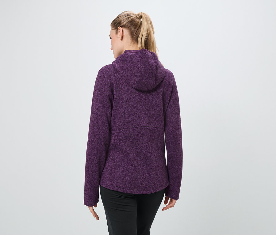 Vue de dos, une femme aux cheveux blonds attachés en queue de cheval porte un sweat à capuche violet et un pantalon noir.