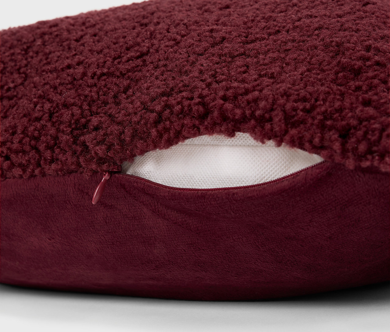 Détail d'un coussin bordeaux duveteux avec une fermeture éclair.