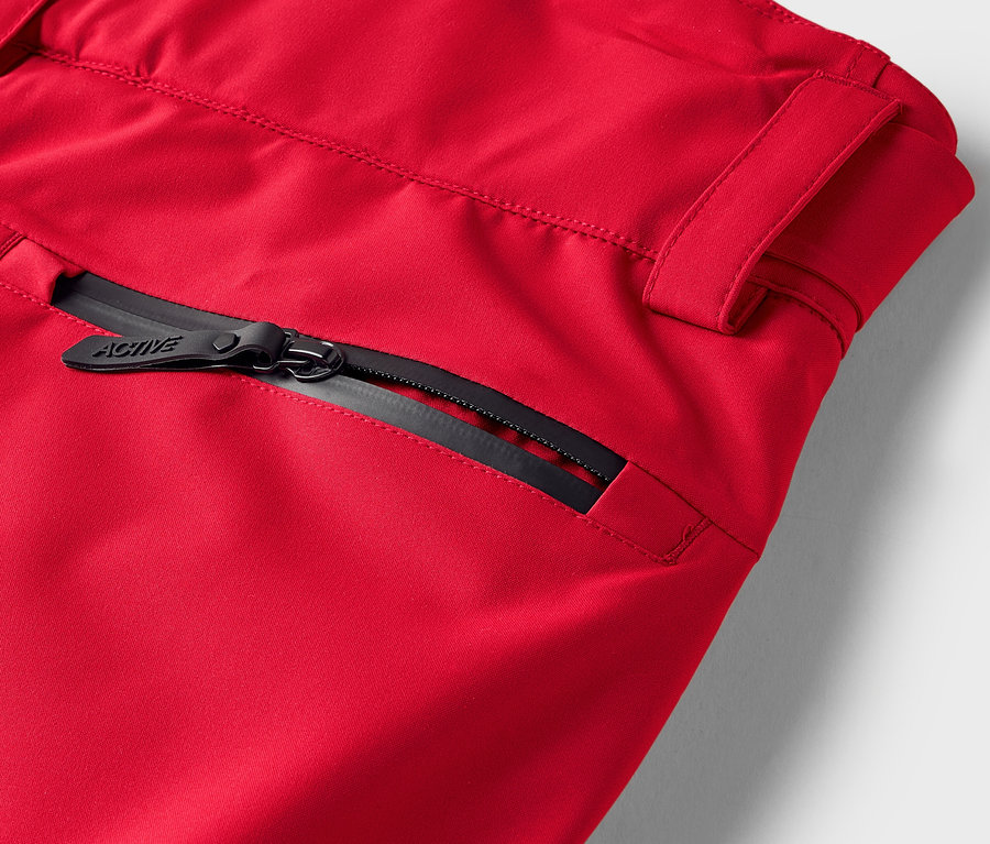 Détail d'un pantalon rouge avec une fermeture éclair noire sur la poche.