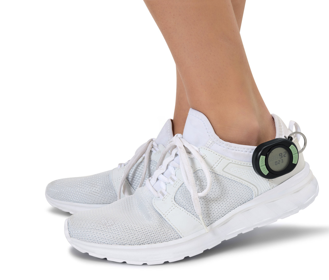 Pieds en chaussures blanches avec un podomètre noir attaché au talon d'une chaussure.