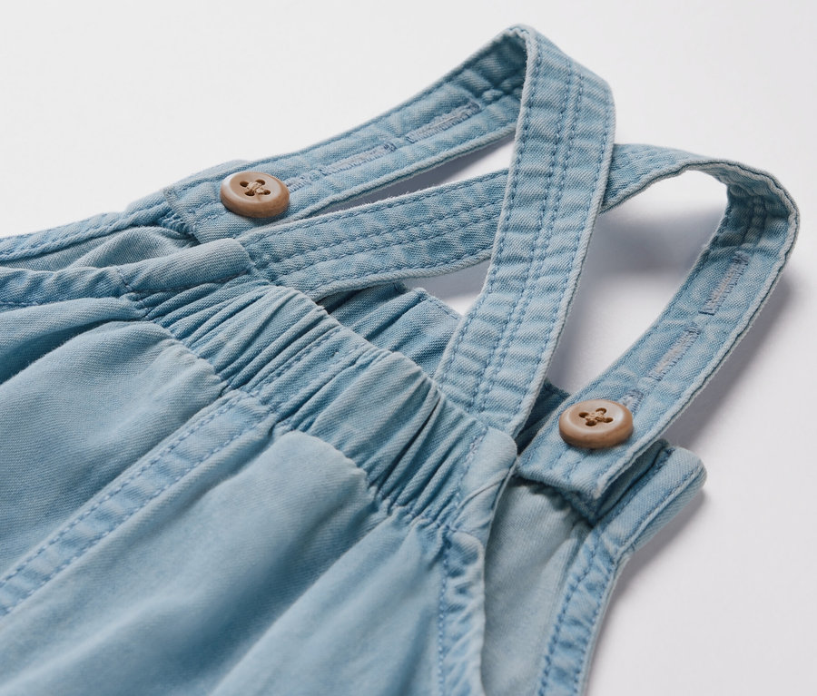 Gros plan sur une salopette en chambray pour enfant avec des boutons en bois.