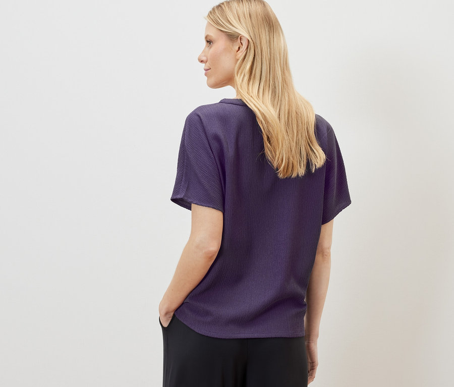 Une femme blonde porte un chemisier à manches courtes structuré et un pantalon noir.