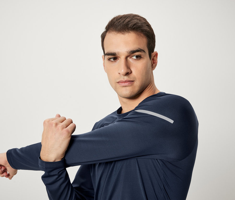 Un homme étire son bras dans un t-shirt de sport à manches longues bleu marine.